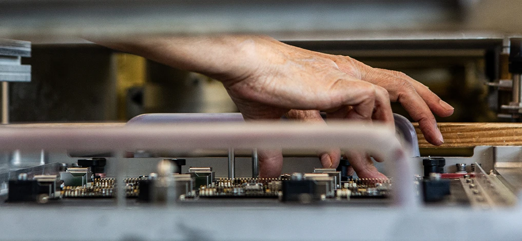 Cette image montre des mains assemblant un PCB avec des composants THT, le préparant pour le processus de soudure à la vague. Elle illustre le travail manuel méticuleux impliqué dans les processus de fabrication électronique chez Cloos Electronic.