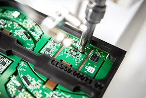 Un robot de soudage achève une carte électronique issue de l'assemblage SMD en soudant des broches pogo (composants THT). La précision mécanique est assurée par un outil de soudage conçu par CLOOS electronic. Le défi réside dans le positionnement précis d'un PCBA flex-rigide.
